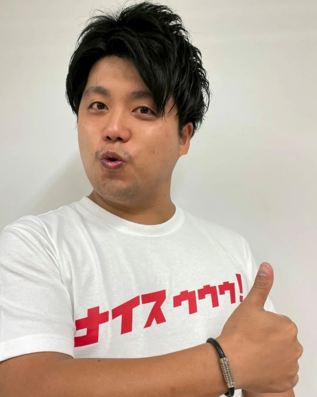 男性が親指を立てており、白いTシャツを着ており、Tシャツには赤い文字で「ナイスゥゥゥ！」と書かれています。