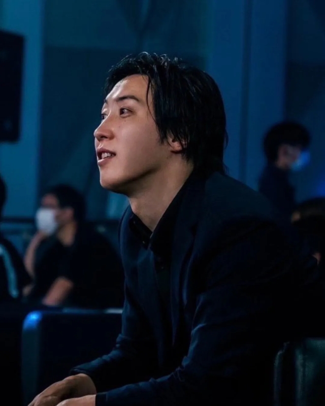 黒いスーツを着た男性のポートレート。彼はカメラから外れて見上げており、他の人が背景にいます。