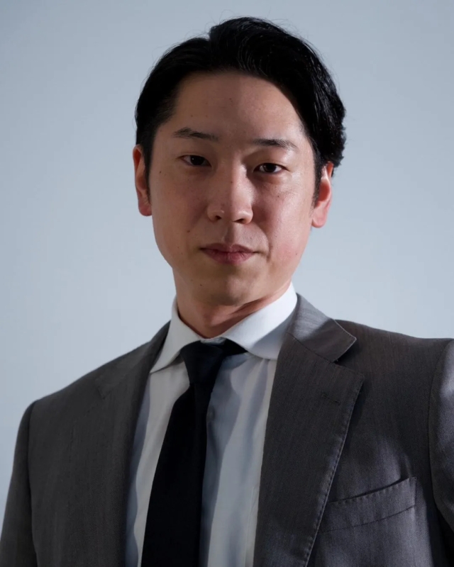 スーツを着たアジア系の男性のポートレートです。彼はカメラを真っ直ぐ見ています。