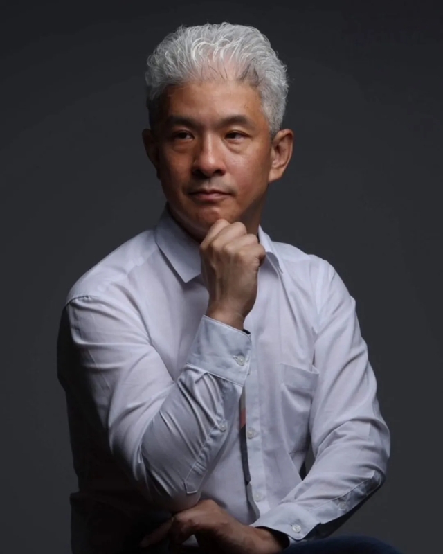 白髪の男性が、顎に手を当てて考え込んでいるポートレート写真。